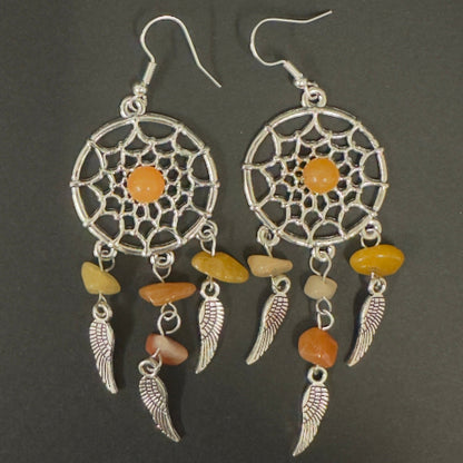 Pair of dreamcatcher earrings with orange and beige stones on a dark background