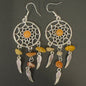 Pair of dreamcatcher earrings with orange and beige stones on a dark background