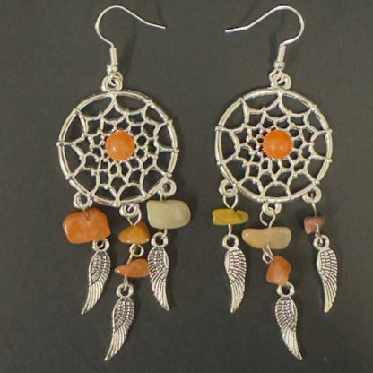 Pair of dreamcatcher earrings with orange and beige stones on a dark background