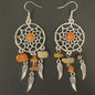 Pair of dreamcatcher earrings with orange and beige stones on a dark background