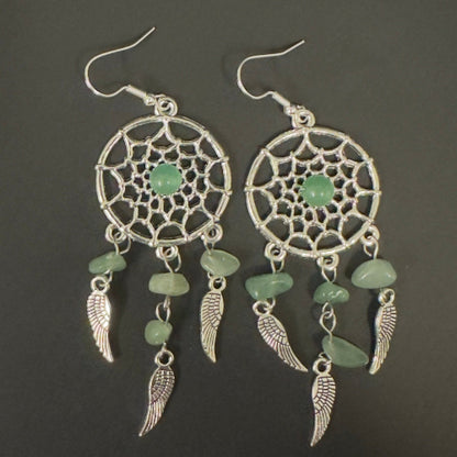 Pair of dreamcatcher earrings with green stones on a dark background
